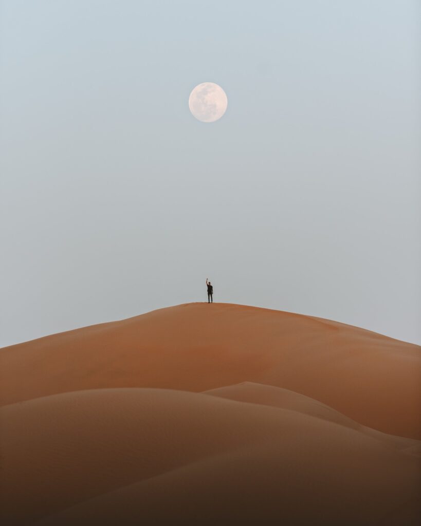 Person standing on dune under the Moon.