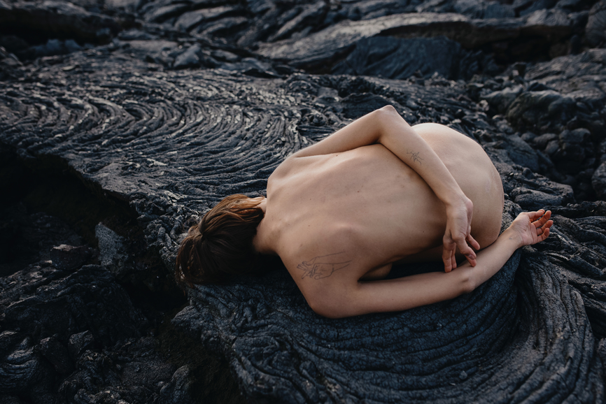 Naked person curled up on a cooled black volcanic flow.